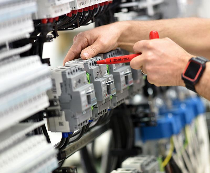 An electrician tightening connections in a circuit breaker cabinet